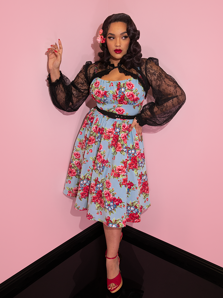 Ashleeta with flowers in her hair modeling the Vixen Clothing Ingenue dress in blue and red rose print paired with a black lace bolero.