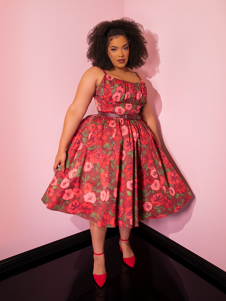 Model standing in the corner of a room posing in the Ingenue Dress in Chocolate Rose Print from Vixen Clothing.