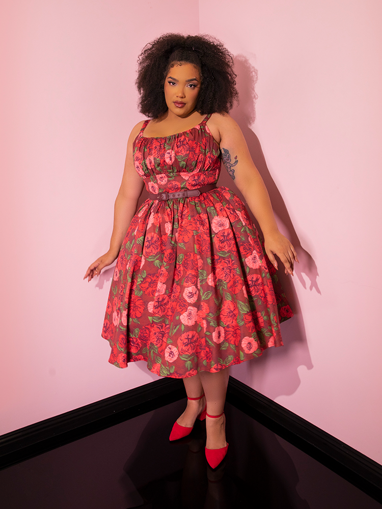 Model posing in the corner of a pink showroom while wearing the Ingenue Dress in Chocolate Rose Print.