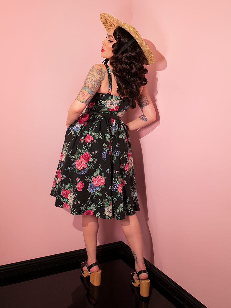 Micheline Pitt turned away from the camera to show off the back of the Ingenue Dress in Black Rose Print from retro dress company Vixen Clothing.