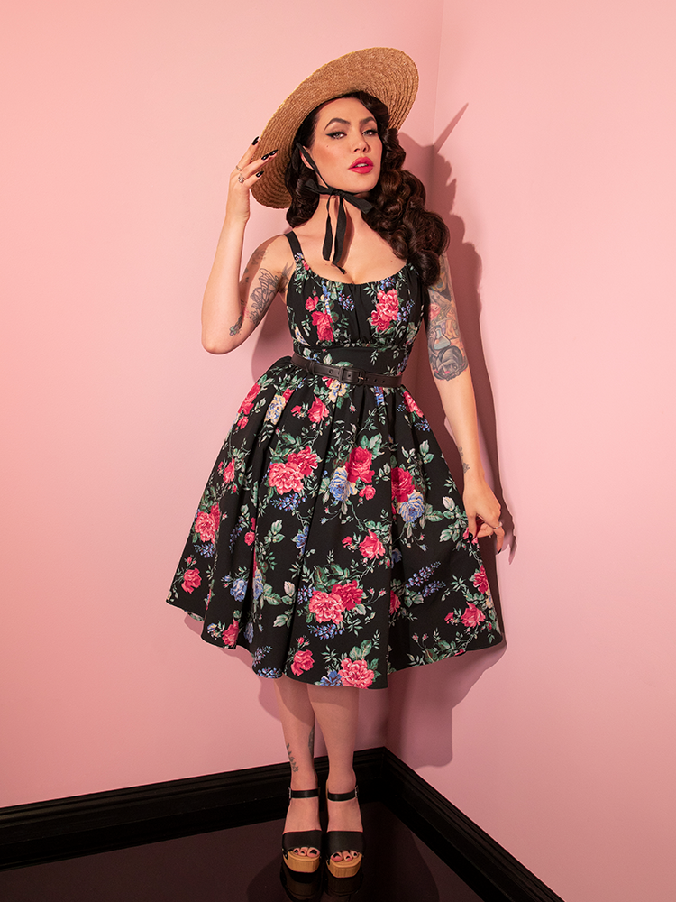 Full length shot of Micheline Pitt in a black retro style dress with a colorful floral print.