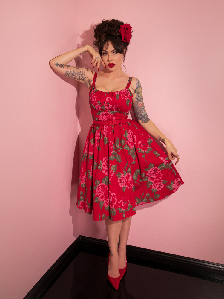 Micheline Pitt pulling the skirt of her Ingenue Swing Dress in Vintage Red Rose Print to reveal the intricate red rose design.