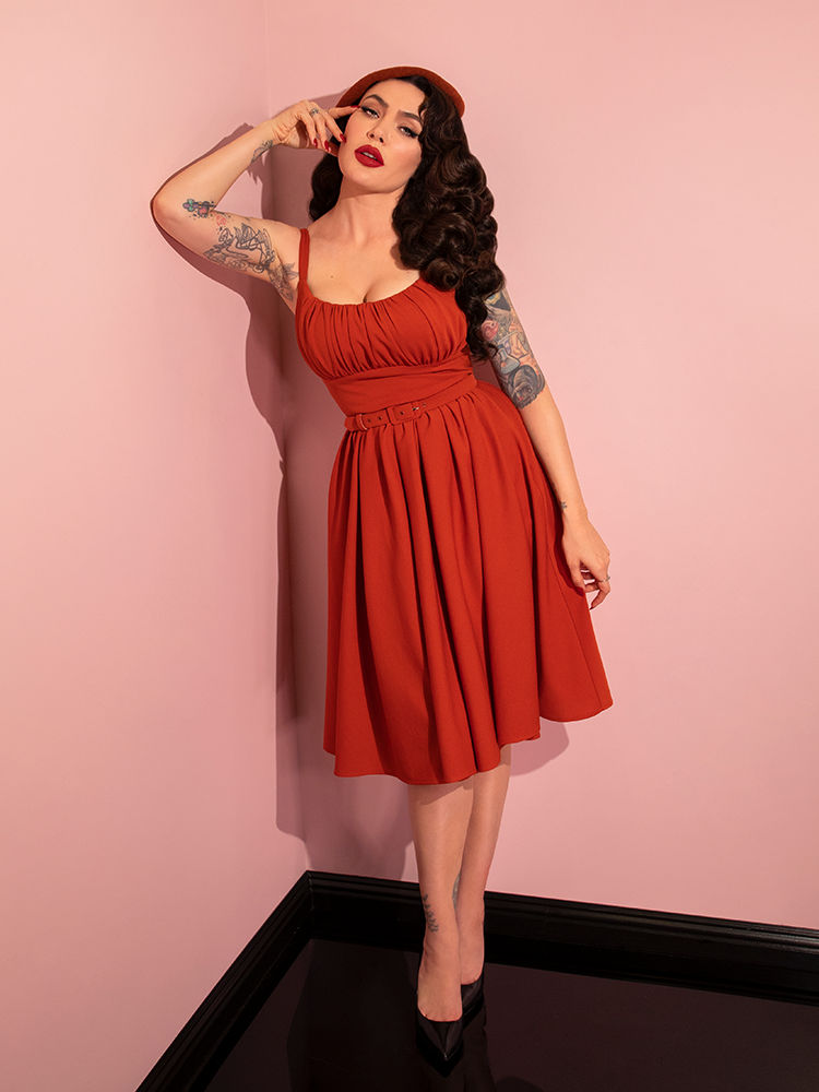 Micheline Pitt strikes a contemplative pose while wearing the Ingenue Swing Dress in Pumpkin Spice from Vixen Clothing.