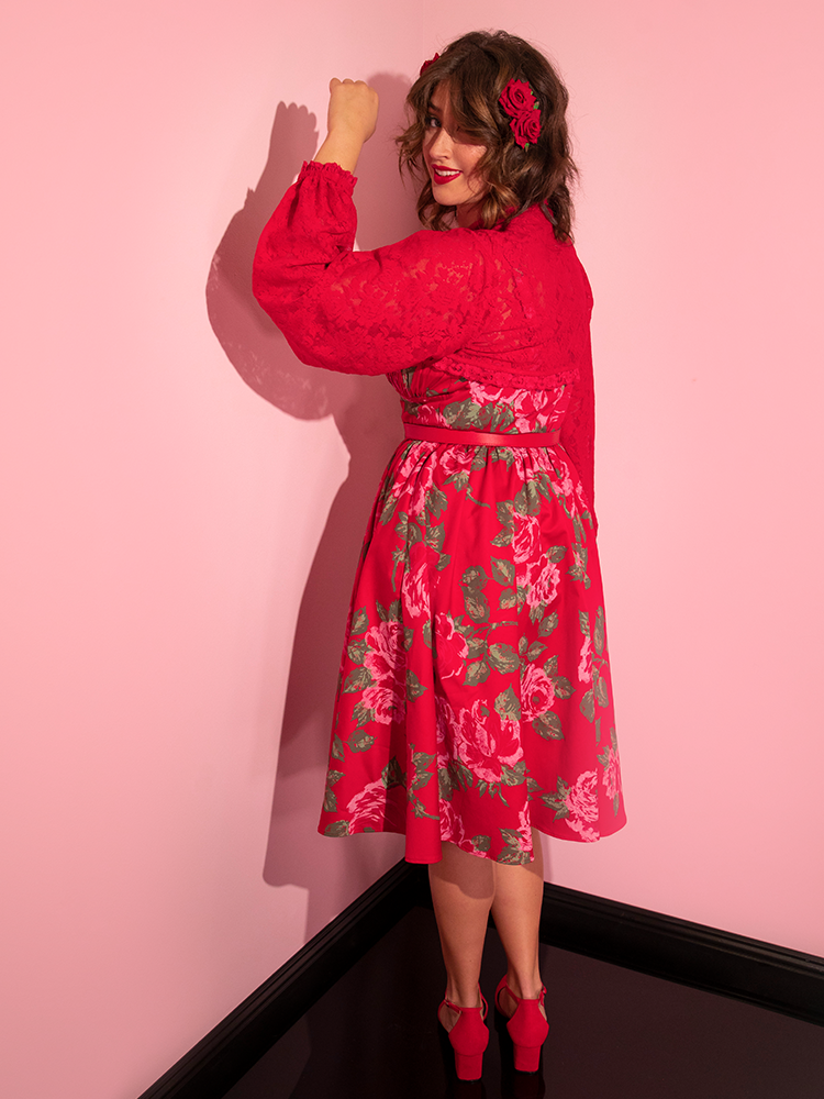 Francesa facing away from the camera while putting her left fist up in the air wears the Ingenue Swing Dress in Vintage Red Rose Print from Vixen Clothing.