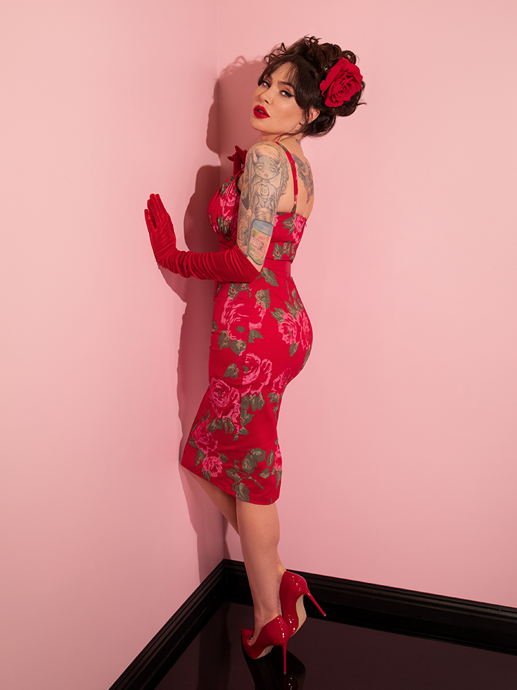 Micheline Pitt turns toward the wall and gives a profile view of the Ingenue Wiggle Dress in Vintage Red Rose Print.