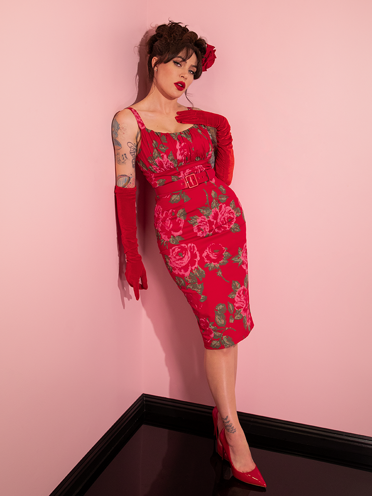 Micheline Pitt leans against the wall while wearing the Ingenue Wiggle Dress in Vintage Red Rose Print.