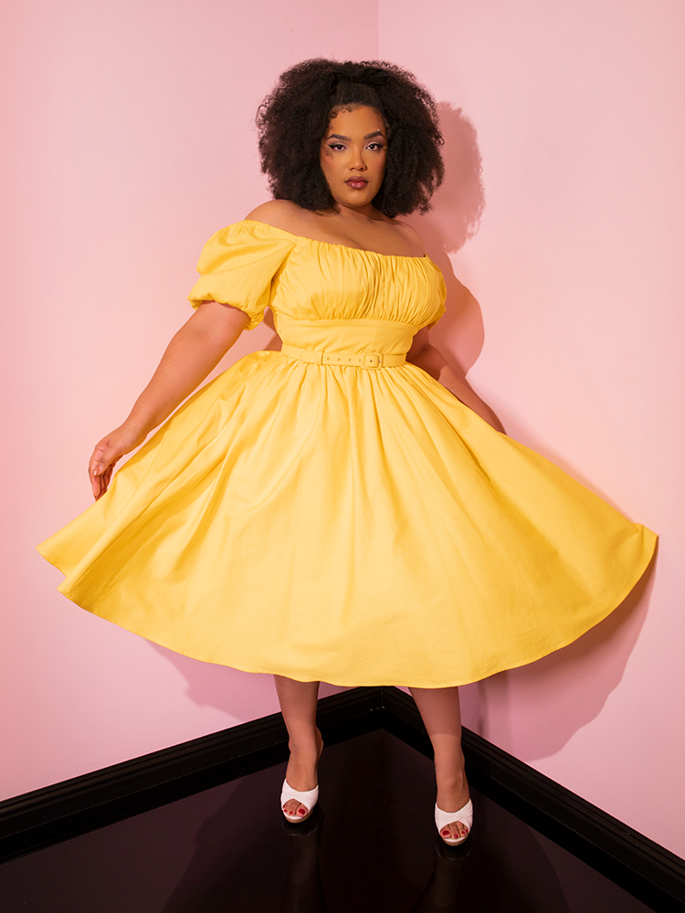 Model twirls around in the Lakeland Dress in Yellow from Vixen Clothing.