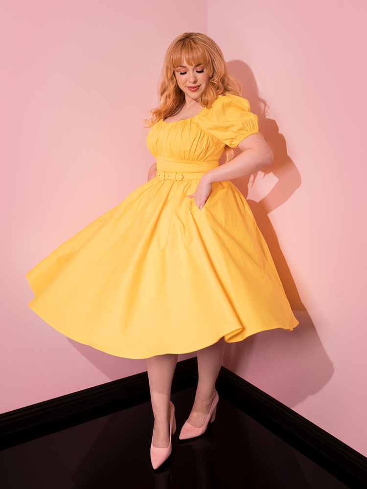 Model twirls around in the Lakeland Dress in Yellow from retro clothing brand Vixen Clothing.