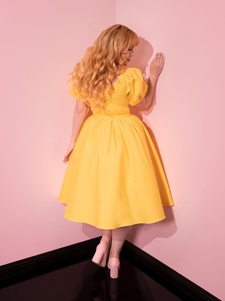 Turned away from the camera, our model gives us a glimpse of the back of the Lakeland Dress in Yellow.
