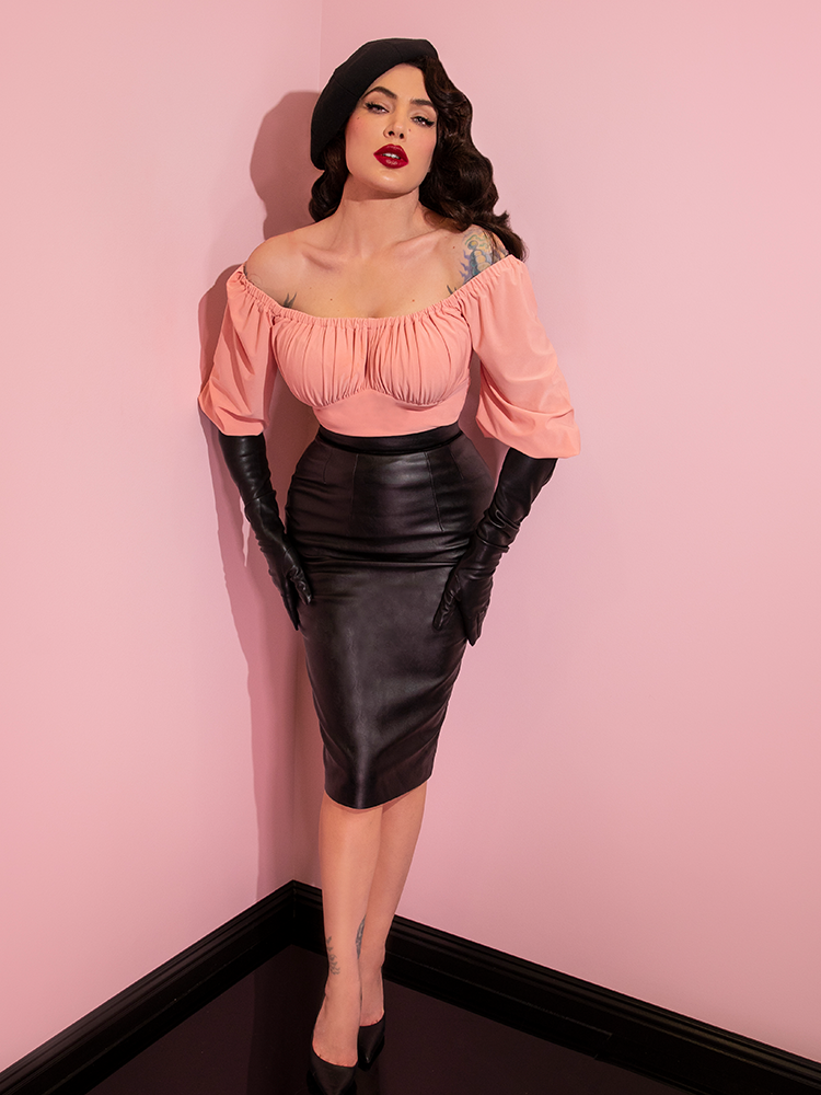 Micheline Pitt wearing a black beret, pink top, and elbow length gloves modeling the Vixen pencil skirt in vegan leather.