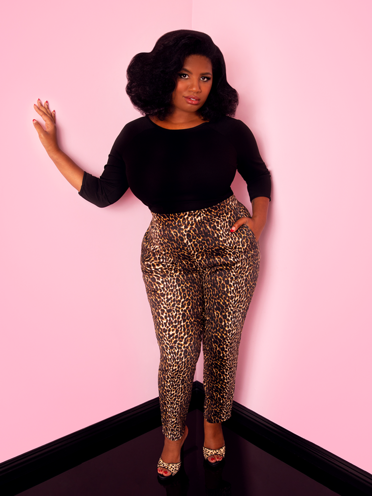 A full length shot of Aretina with her hand in her pocket modeling the cigarette pants in leopard print by Vixen Clothing paired with a black top.