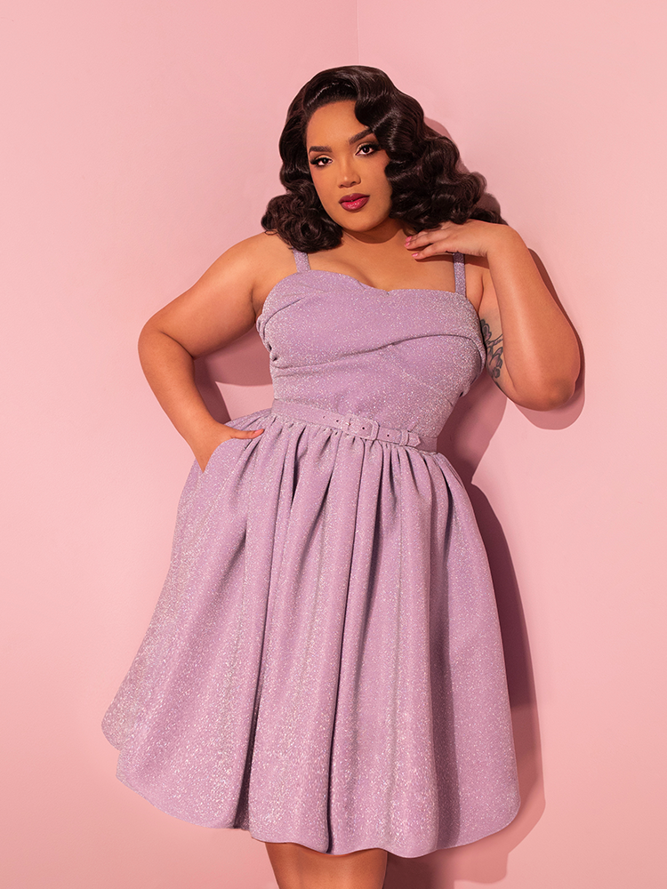 Exuding timeless charm, the lovely female strikes a pose in the Jawbreaker Swing Dress in Lilac Lurex, a captivating creation by Vixen Clothing, the renowned retro dress clothing brand.