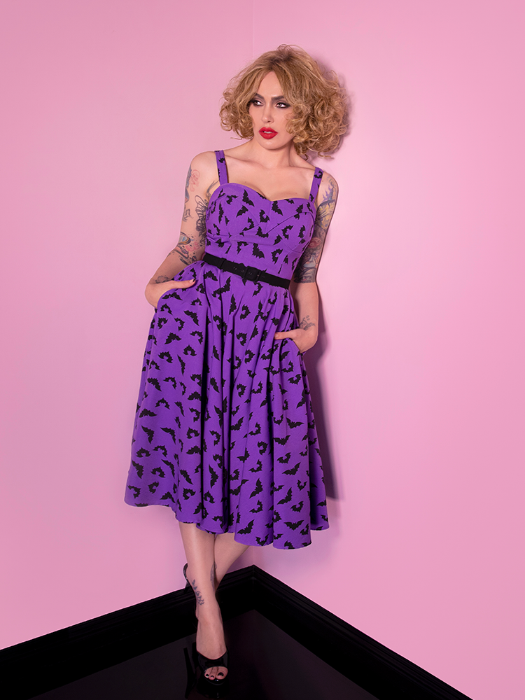Full length image of Micheline Pitt wearing a purple retro style dress.