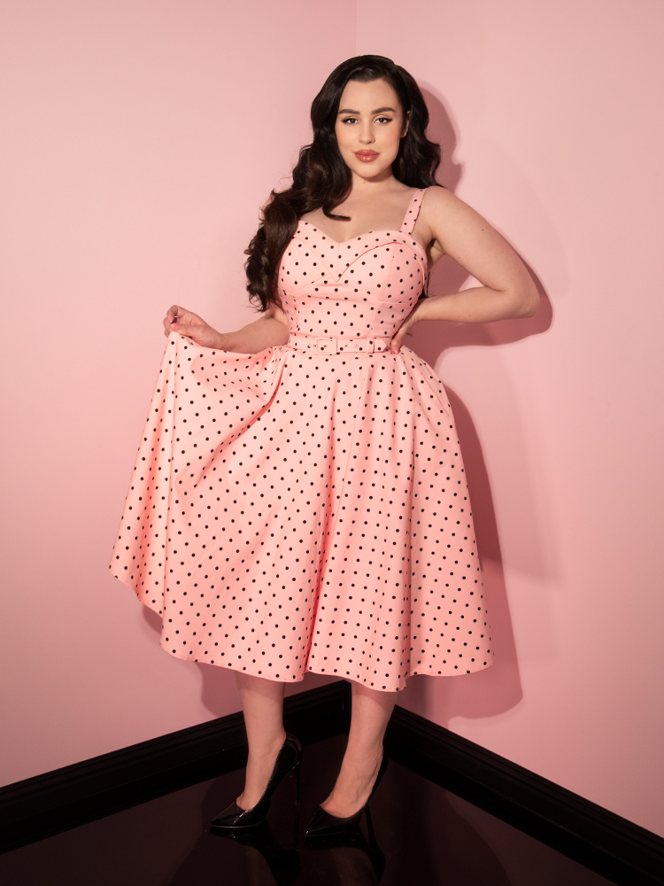 Rachel Sedory holding up the fabric on her skirt to show off the print on the Maneater Swing Dress in Rose Pink Polka Dot.