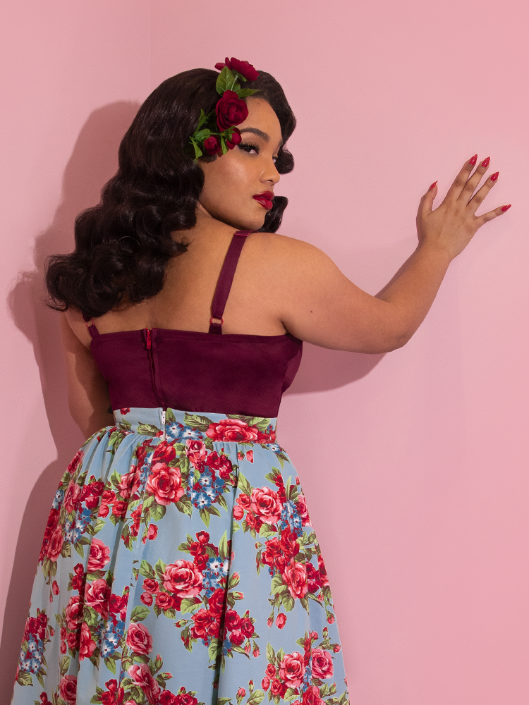 A closeup of Ashleeta looking over her shoulder modeling the Vixen Clothing Maneater top in dark berry paired with hair flowers and a blue floral skirt.