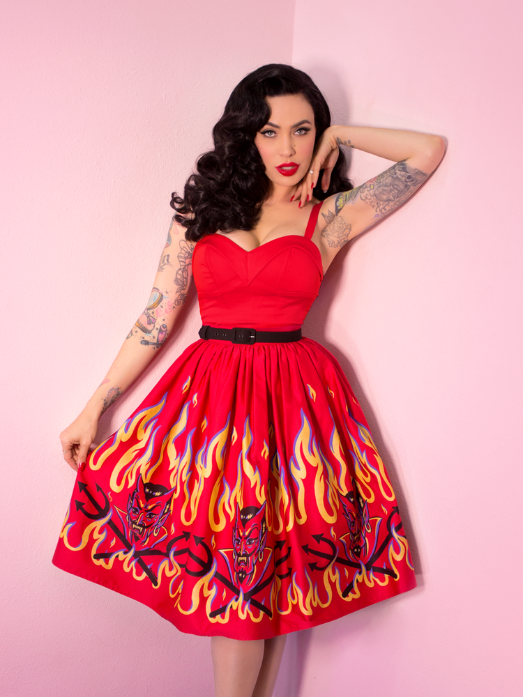 Micheline Pitt with her hand framing her face modeling the Maneater top in red by Vixen Clothing paired with a red flame print skirt.