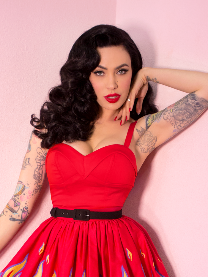 A closeup of Micheline Pitt with her hand framing her face while modeling the Maneater top in red by Vixen Clothing.