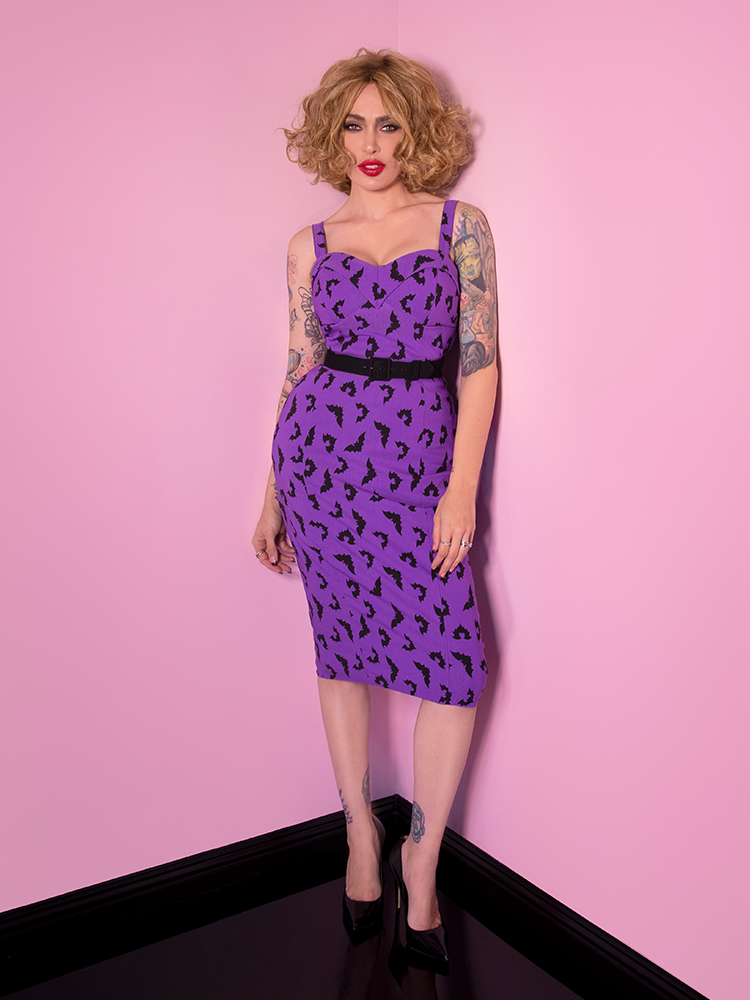 Wearing a purple retro style dress, Micheline stares intently into the camera.