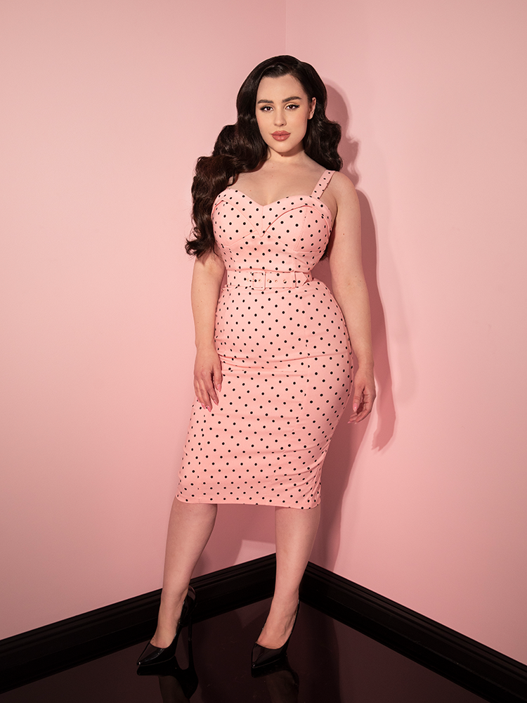 Rachel Sedory posing in her Maneater Wiggle Dress in Rose Pink Polka Dot in front of pink walls.