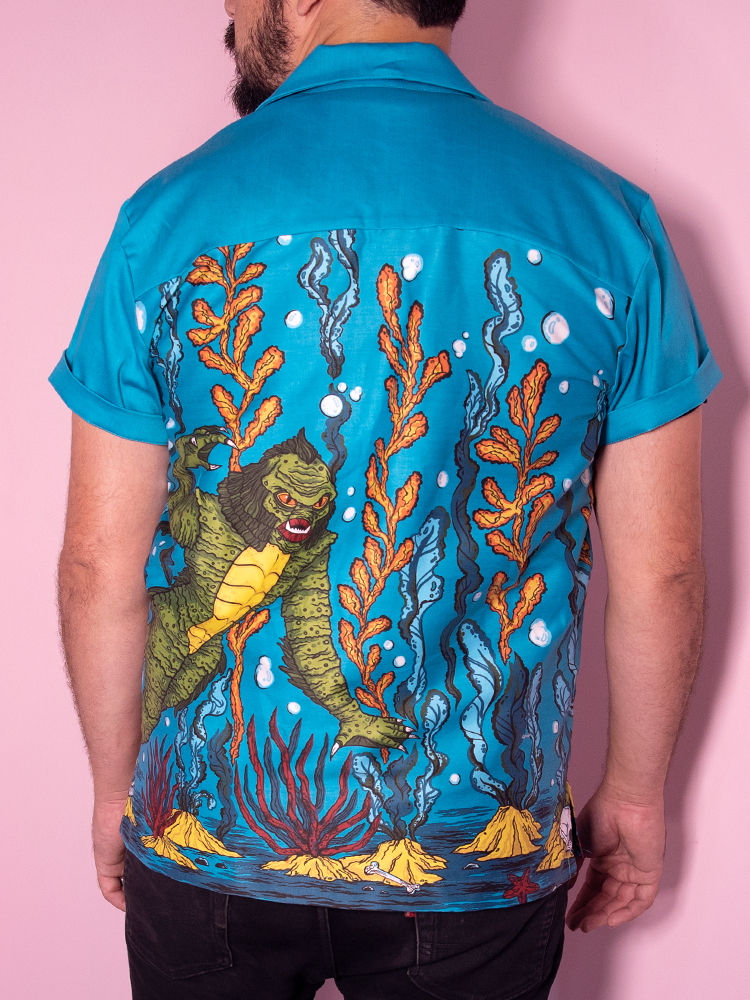 Back view of male model wearing the creature retro shirt from Vixen Clothing. It features an ocean scene with a swamp creature swimming.