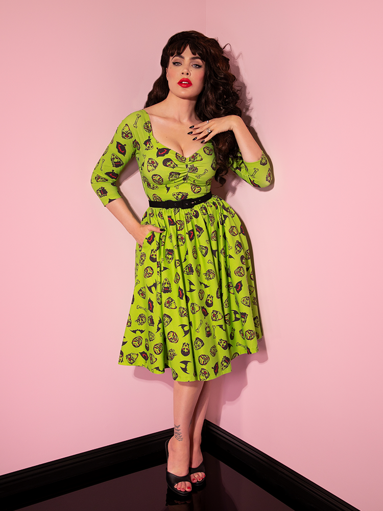 A full length shot of Micheline Pitt posing in the Wicked Swing Dress in Vintage Monster Mash Print with one hand tucked into her pocket.