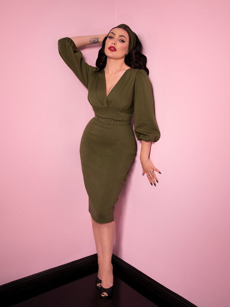 Micheline Pitt looking at the camera modeling the Bawdy wiggle dress in olive green paired with a matching headband.