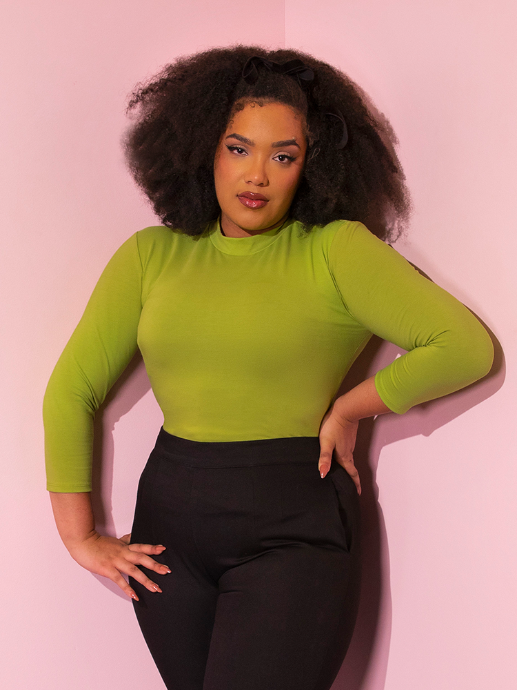Model posing with her hands placed on her hips wears the  Bad Girl 3/4 Sleeve Top in Avocado Green from Vixen Clothing.