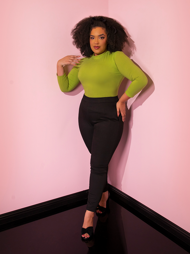 Full length shot of Micheline Pitt wearing the  Bad Girl 3/4 Sleeve Top in Avocado Green tucked into black cigarette pants.