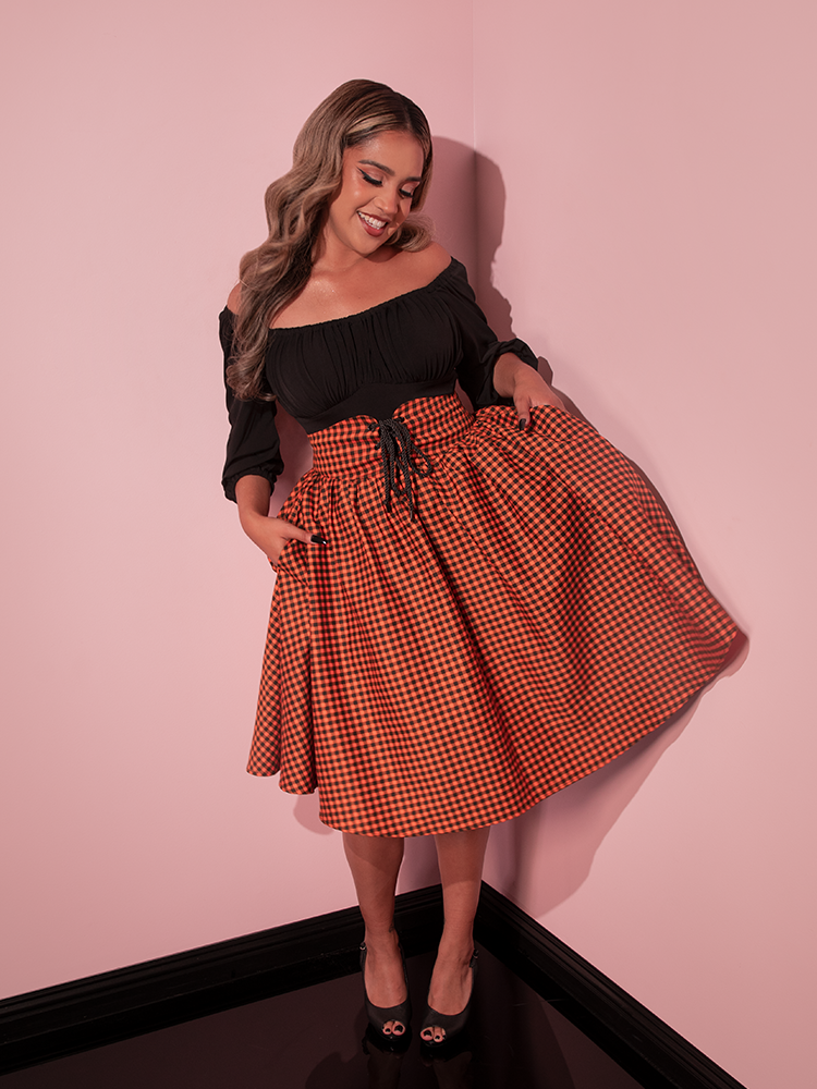 Female model swaying in the Corset Skirt in Orange Pumpkin Gingham with complementary black long sleeve retro top.