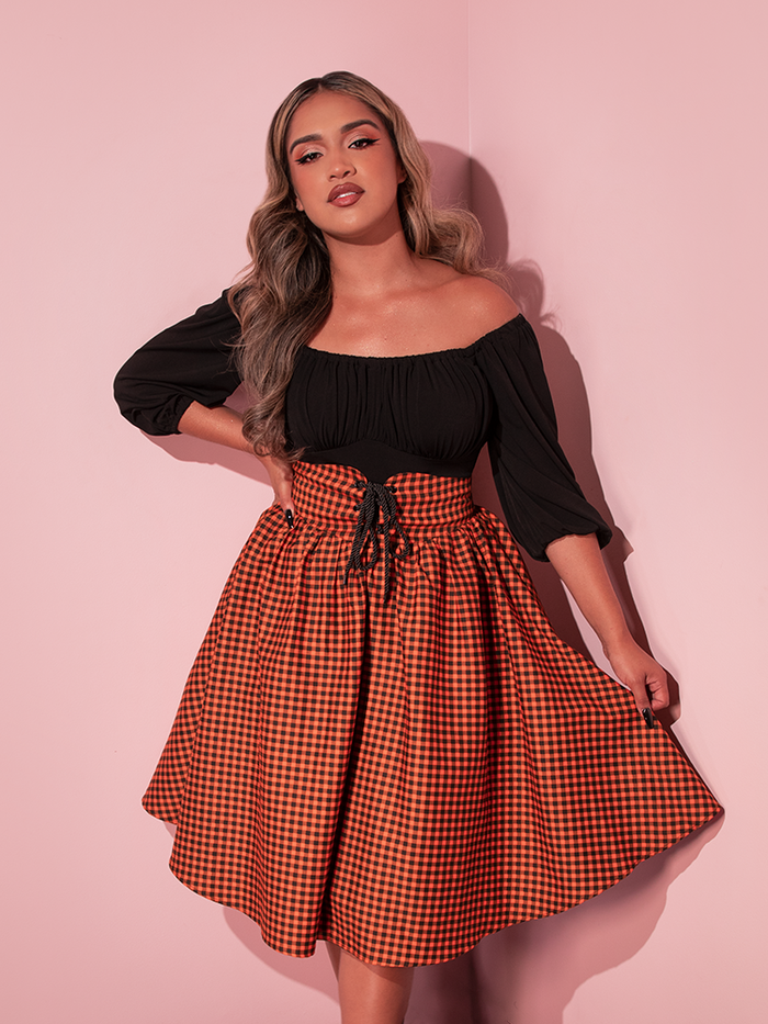 Model gently pulls out the left side of the skirt section of the Corset Skirt in Orange Pumpkin Gingham to model the classically festive print.