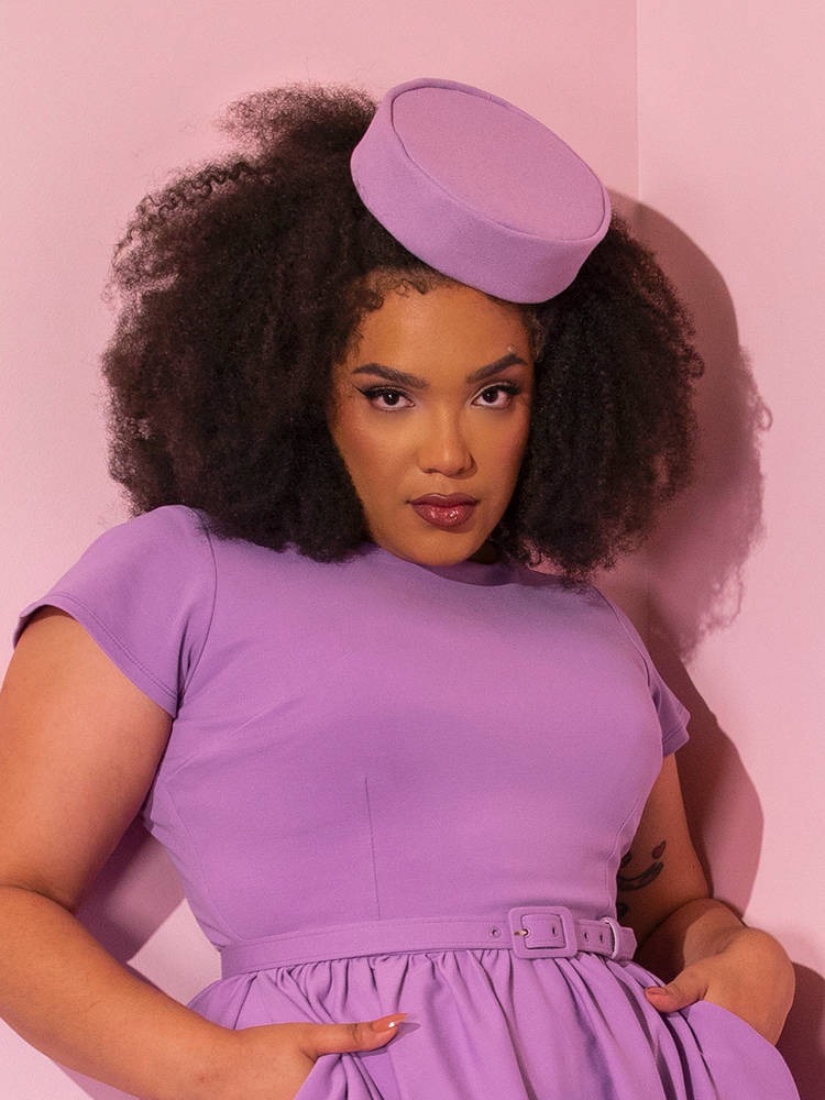 Model wearing a lilac colored retro dress complemented by the Vintage Pillbox Hat in Lilac.
