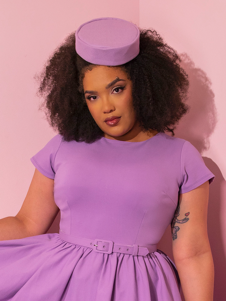 Model stares intently into the camera while wearing the Vintage Pillbox Hat in Lilac.