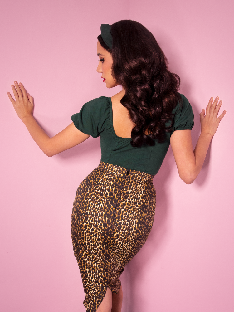 A back view of Milynn modeling the Powder Puff top in hunter green paired with a leopard pencil skirt.