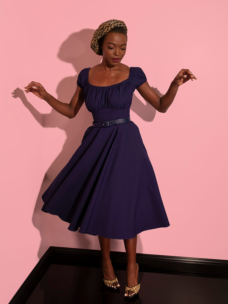 Full length image of model twirling while wearing the Peasant Swing Dress in Navy. 