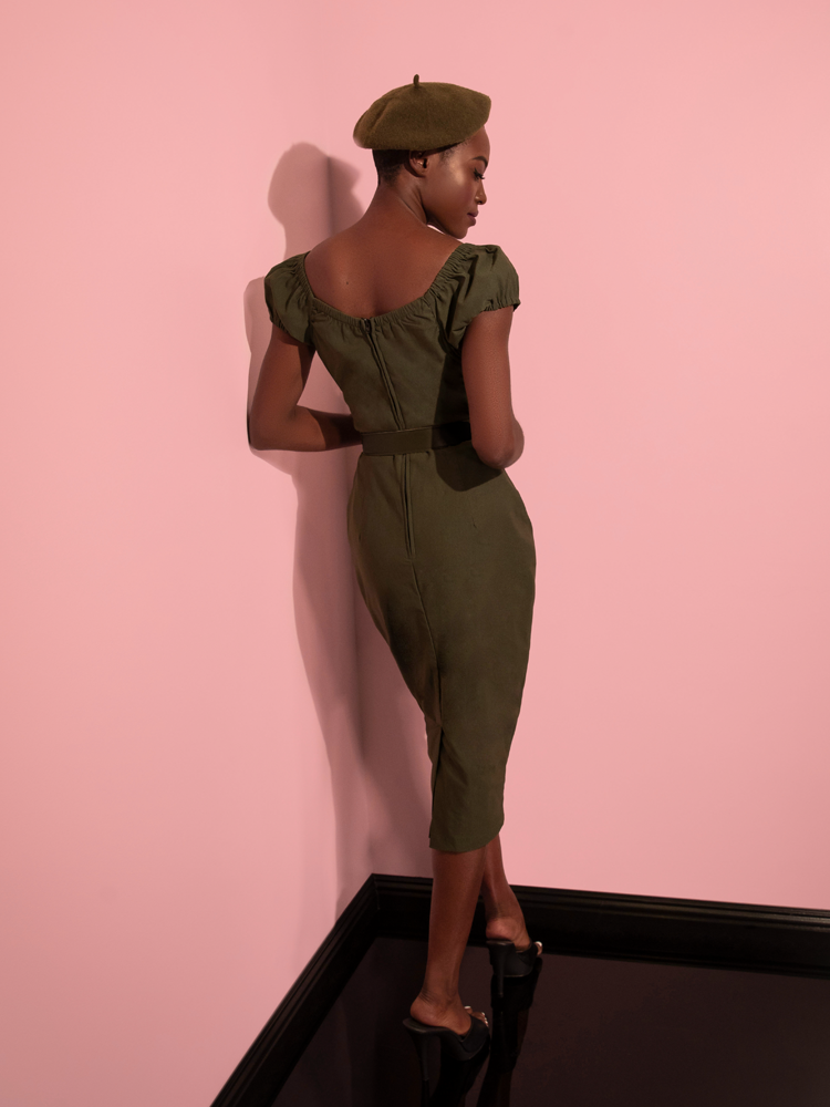 Model turns around to show off the back of the Peasant Wiggle Dress in Olive Green with matching color beret and black shoes.