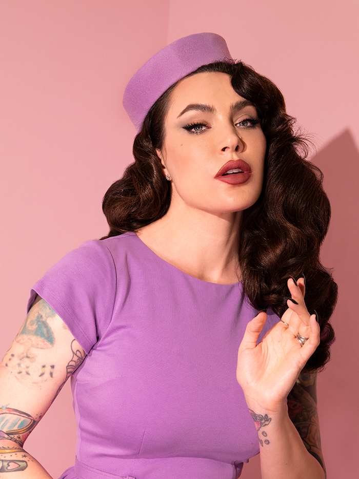 Close-up shot of Micheline Pitt wearing an all lilac colored outfit highlighted by the Vintage Pillbox Hat in Lilac.