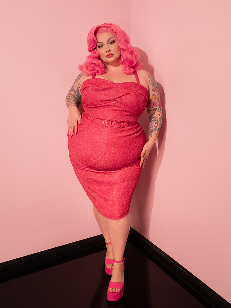 With an air of allure, the female model effortlessly captivates attention as she showcases the Candy Pink Lurex Jawbreaker Wiggle Dress by Vixen Clothing, a true gem among their retro clothing designs.