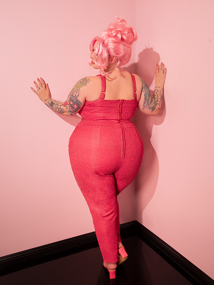 With a captivating retro allure, the gorgeous model confidently flaunts the Cigarette Pants in Candy Pink Lurex from Vixen Clothing, capturing attention effortlessly.
