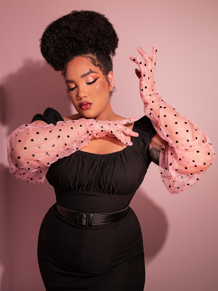 Ashleeta closing her eyes and posing with her arms posed out in front of her to show off the Mesh Polka Dot Full Length Gloves in Rose Pink along with the retro style top she’s tucked into her black pants.