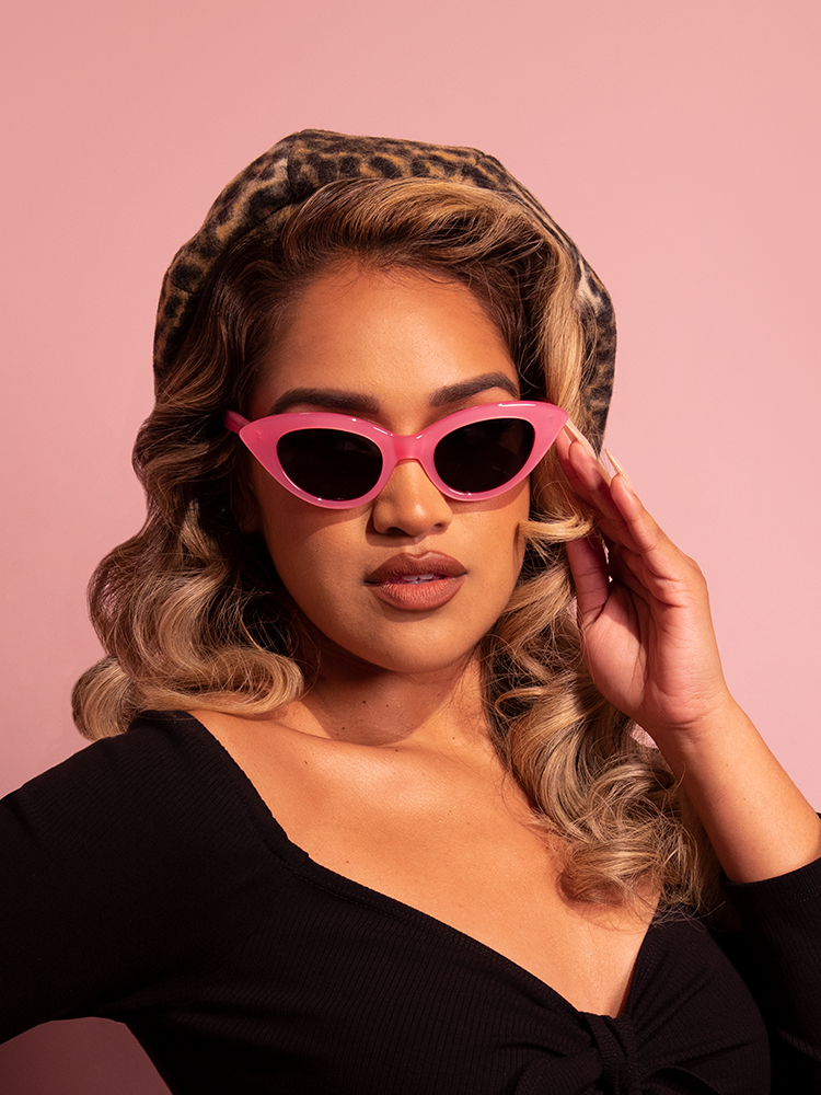 Model posing seductively in the Fashion Doll Cat Eye Sunglasses in Pink with a low cut black retro top on.