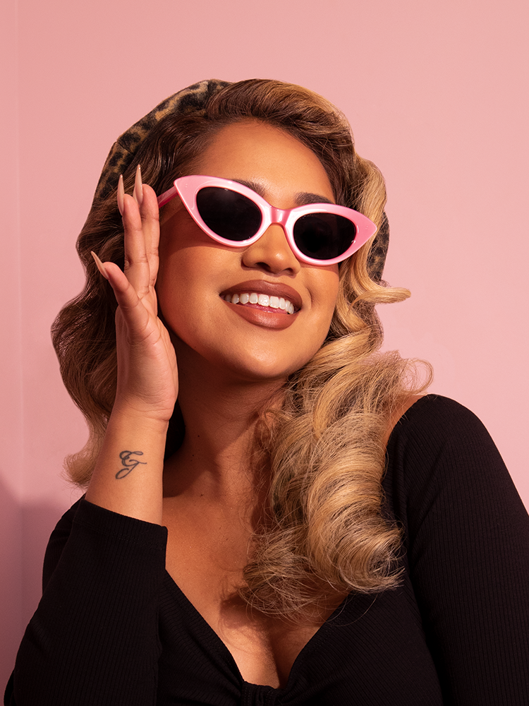The Fashion Doll Cat Eye Sunglasses in Pink worn by tan female model along with black top.