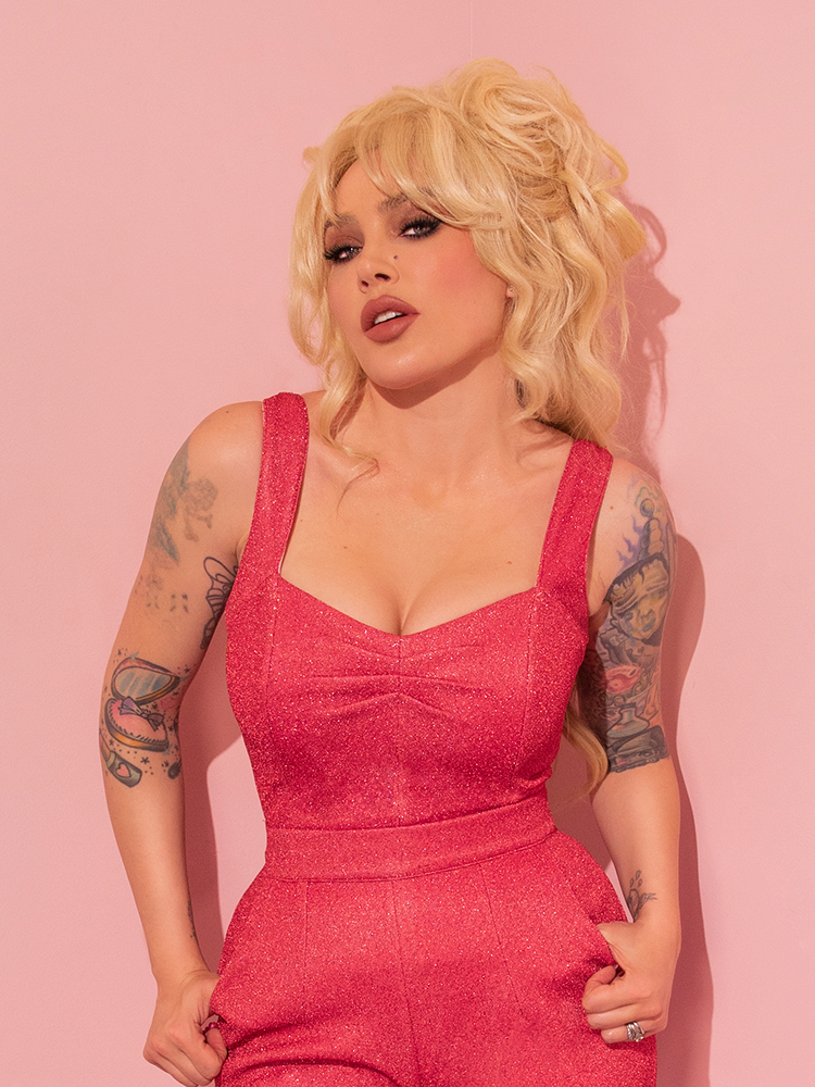 With a touch of nostalgia, the model enthralls in her retro ensemble, drawing attention to the striking Candy Pink Lurex Vamp Top from Vixen Clothing.