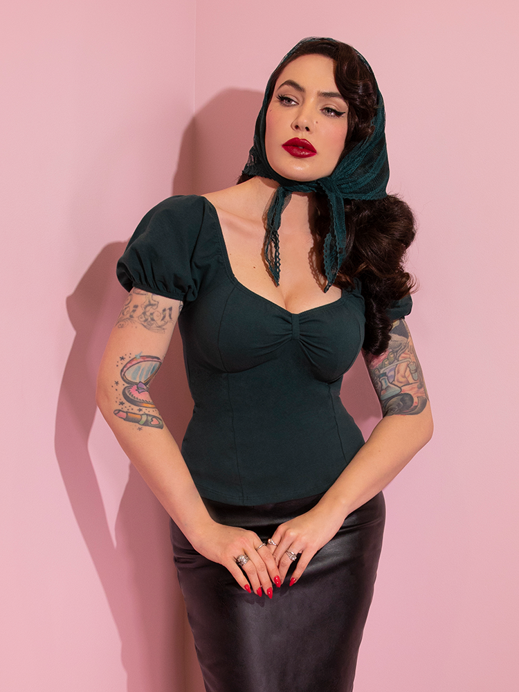 A closeup of Micheline Pitt modeling the Powder Puff top in hunter green untucked paired with a black pencil skirt and green head scarf.