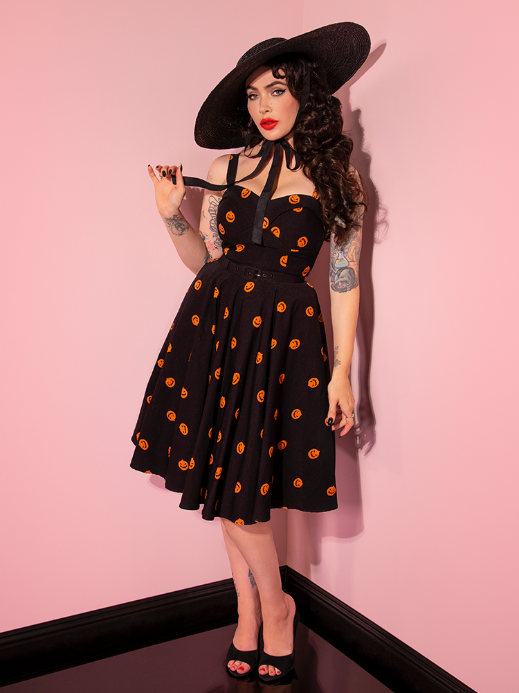 Micheline Pitt pulls on the ties of her black sunhat while she also wears the Pumpkin King Maneater Swing Dress in Black. 