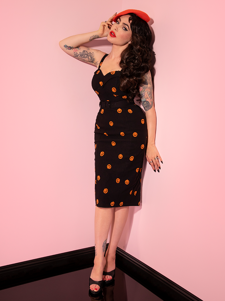 Micheline Pitt leaning against the wall in the Pumpkin King Maneater Wiggle Dress in Black from retro clothing company Vixen Clothing.