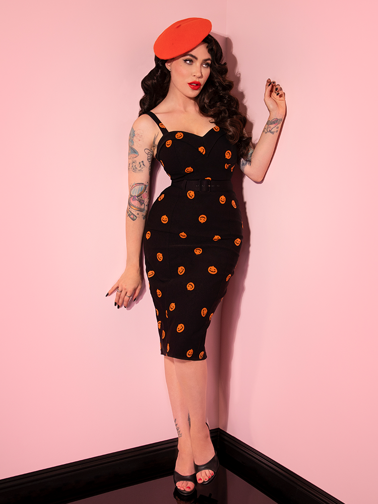 Micheline Pitt staring off camera while wearing the Pumpkin King Maneater Wiggle Dress in Black and orange beret from Vixen Clothing.