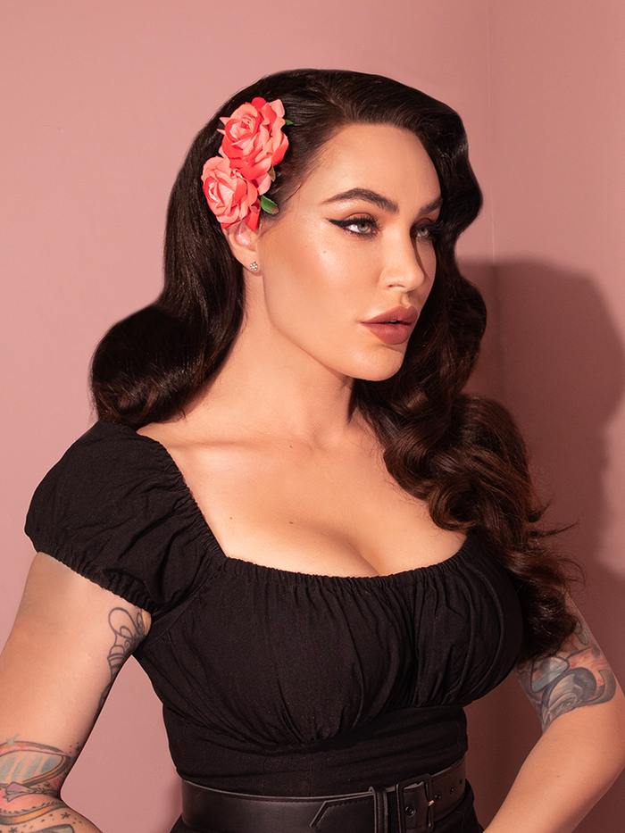 Profile shot of Micheline Pitt wearing the Vintage-Style Double Rose Hair Comb in Pink/Red from retro clothing brand Vixen Clothing.
