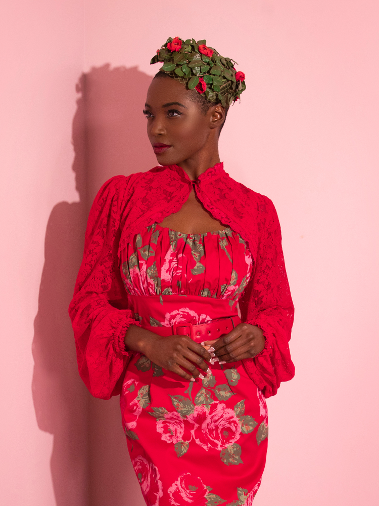 Brittany looks off the side to show the camera her profile while modeling the Vixen Vintage Lace Bolero in Classic Red and matching red rose vintage style dress from Vixen Clothing.