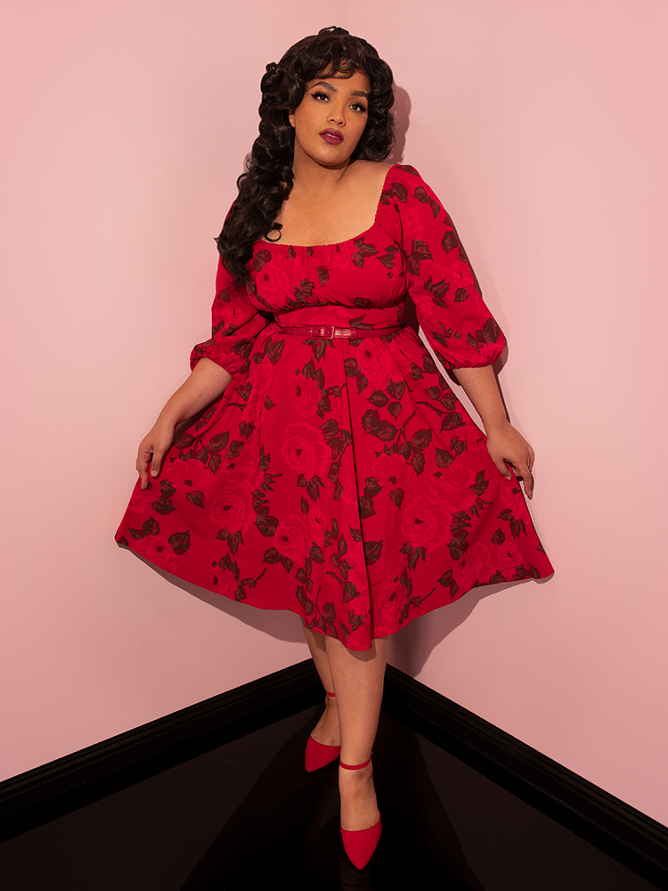 Ashleeta tugging on either sides of the skirt on her Vacation Dress in Vintage Red Rose Print from Vixen Clothing.
