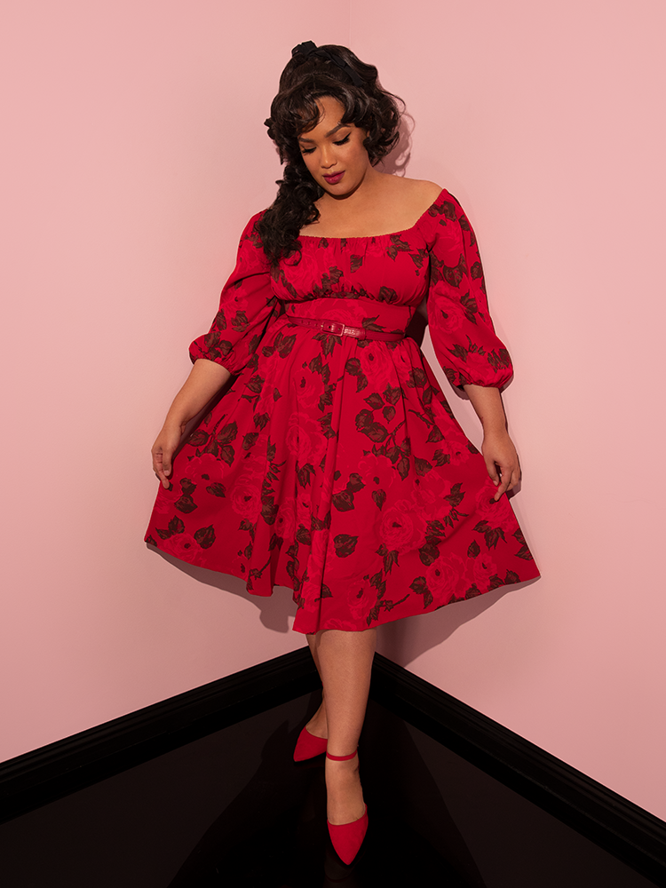 Full length shot of Ashleeta pulling the skirt of the Vacation Dress in Vintage Red Rose Print taut to show off the gorgeous red rose print.